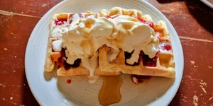 Waffles on a plate whipped cream and strawberries.